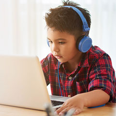 Un enfant avec un casque d'écoute regarde l'écran de son ordinateur.