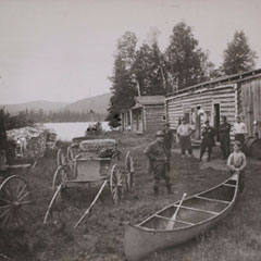 Une carriole, un canoë et des hommes se trouvent devant un chalet.